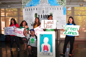 Group chants and hold signs reading San Joaquin Valley, Energy, Land Use, and Green Zones, with a poster showing lungs and reading 34 Prevent Prevenir